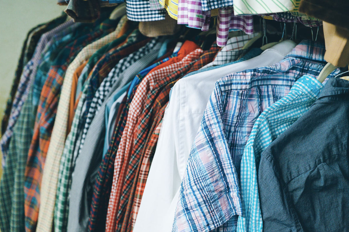 A close-up view of a clothing rack filled with various plaid and checkered button-down shirts in multiple colors, including blue, red, green, orange, and white.