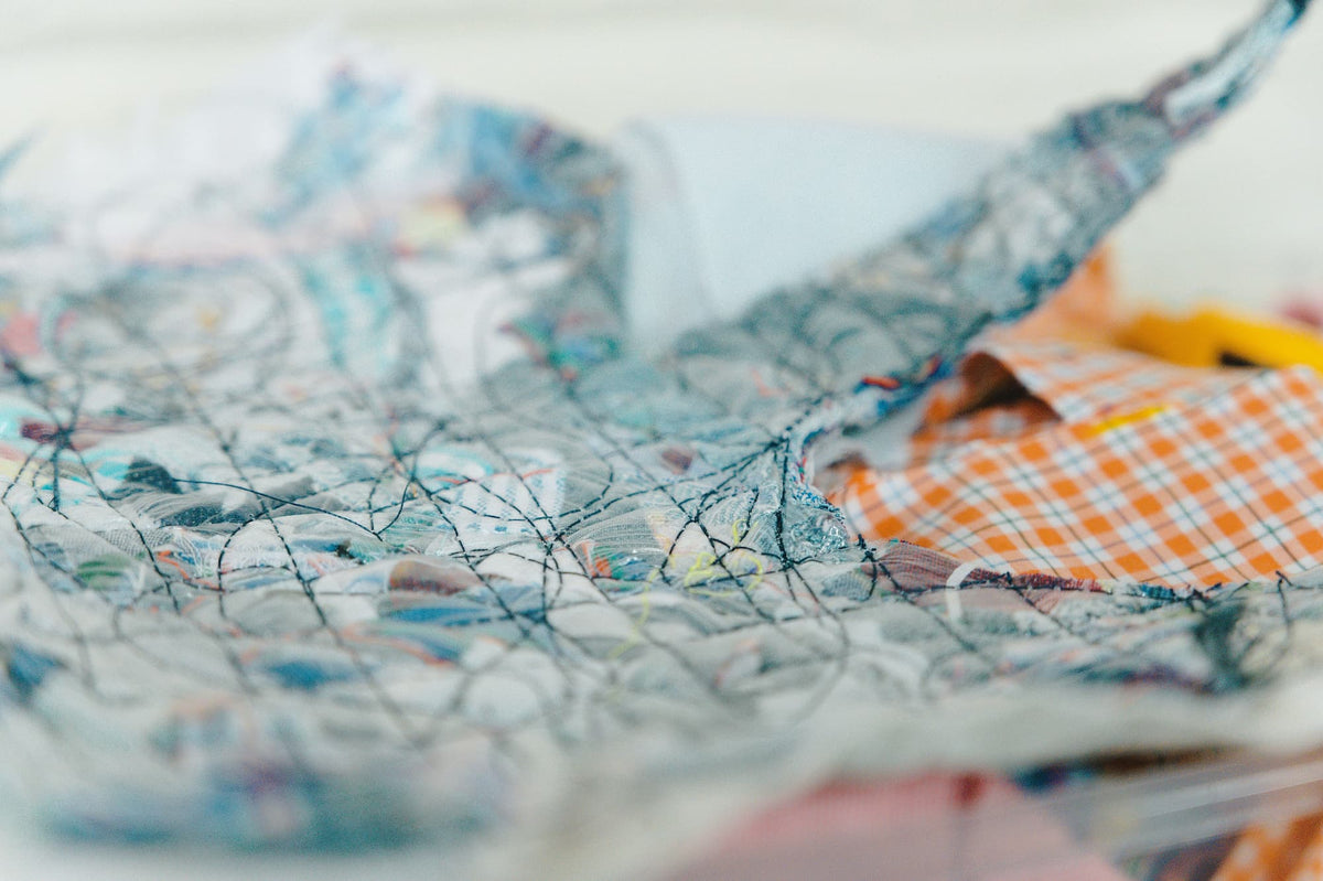 A close-up, shallow depth-of-field shot of a handmade quilted fabric piece, showing intricate stitching and a mix of blue, orange, and white patterned fabrics.