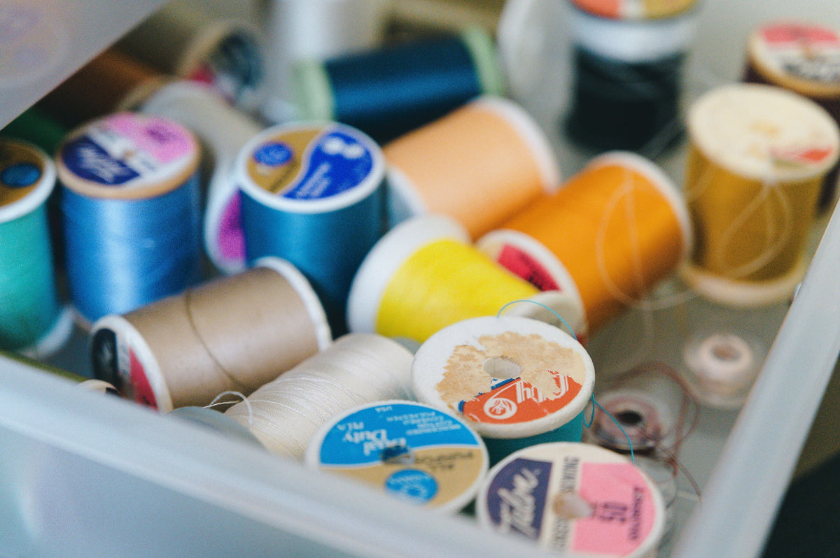 A close-up, slightly blurry view of a drawer filled with multiple spools of thread in various colors including blue, orange, yellow, beige, and white.