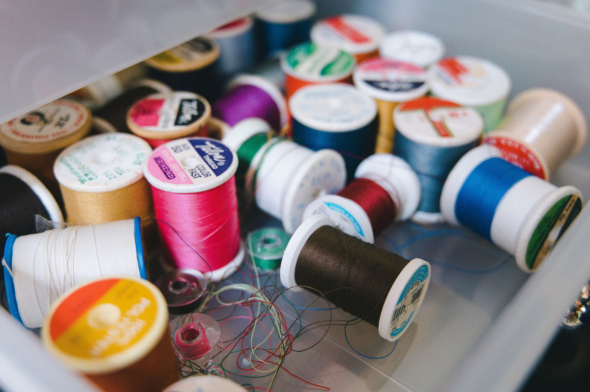 A close-up view of a clear plastic drawer filled with assorted spools of thread in many colors, including pink, blue, green, brown, white, and yellow.