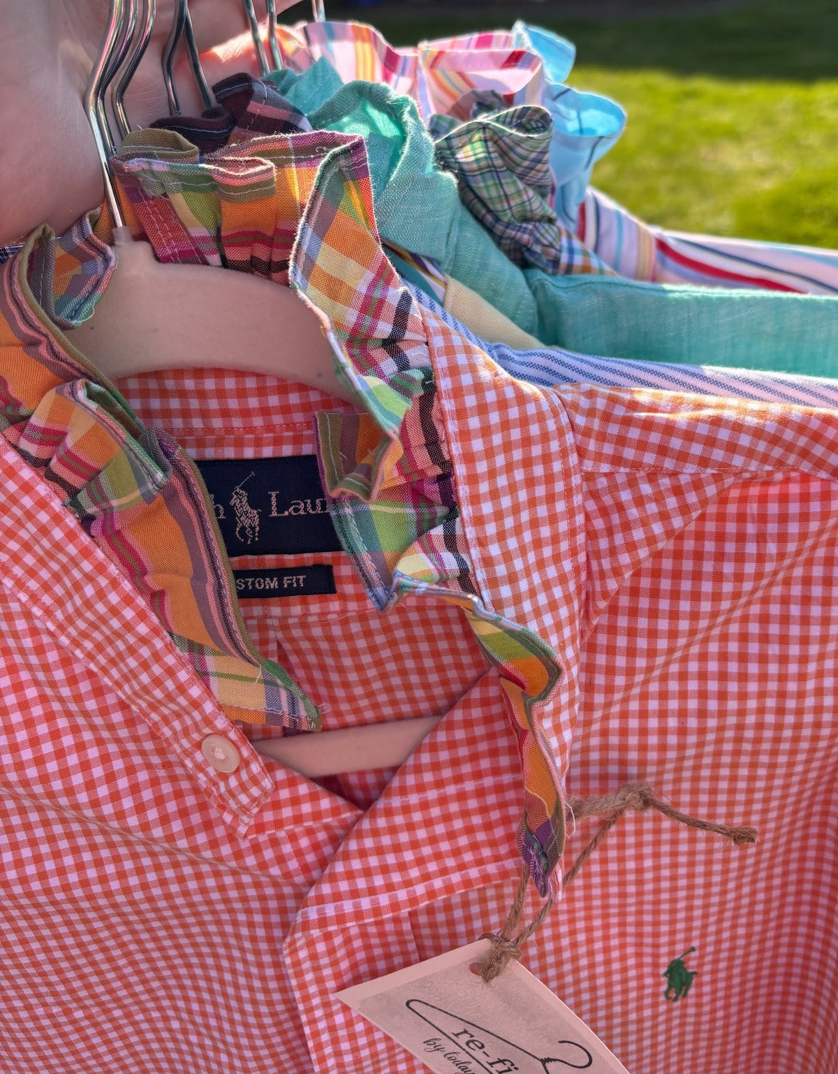 Stack of colorful shirts with Polo Ralph Lauren branding on a grassy background