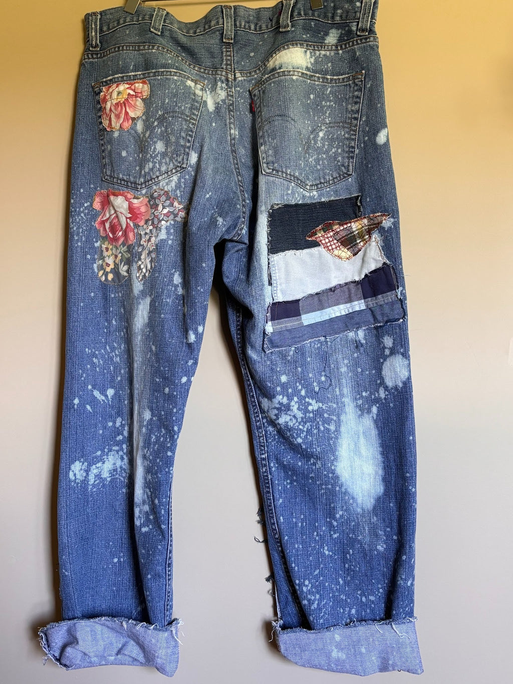 Blue jeans with floral patches and paint splashes on a beige background